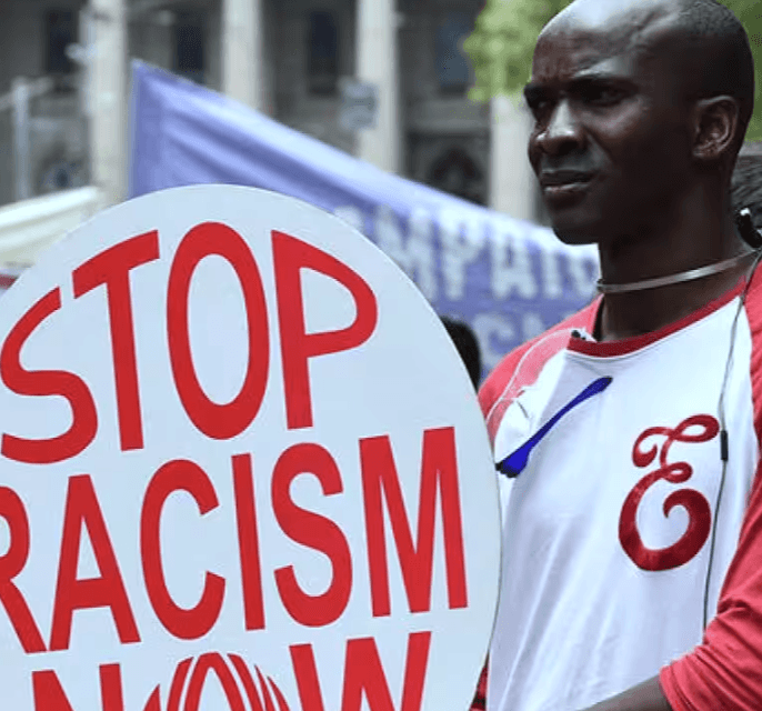 A man at a protest holding a sign that says "Stop Racism Now"